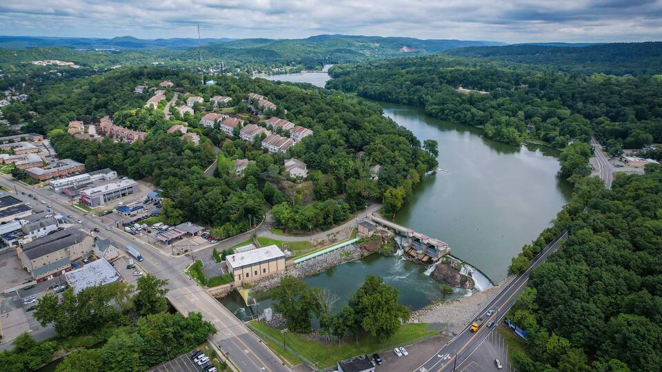 An aerial view of a town with a river, a bridge, and surrounding greenery.