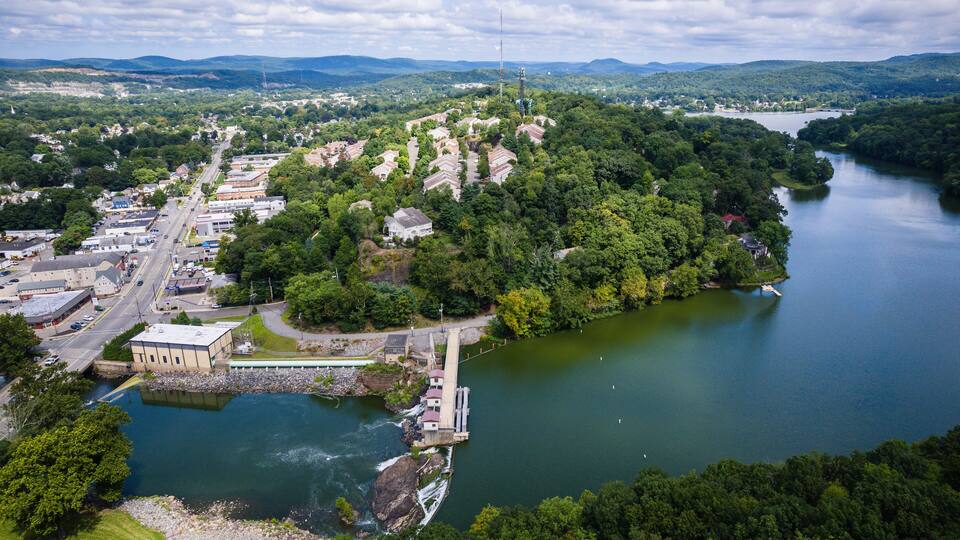 A river with a dam and a town with buildings and greenery.