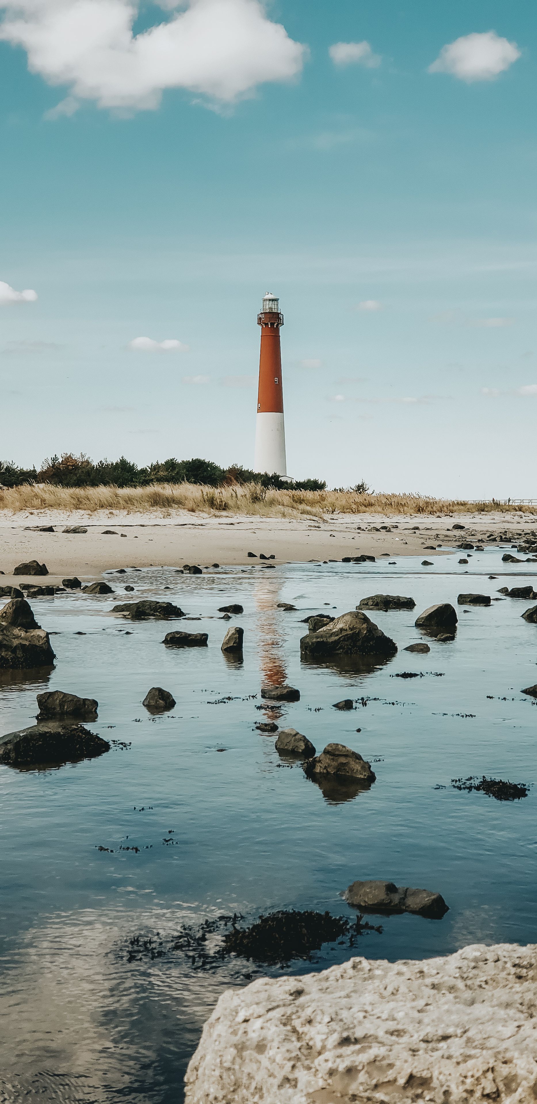 Barnegat Lighthouse reflecting in water with rocks at beach