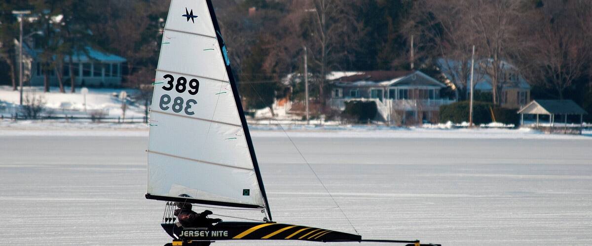 A sailboat with the number 389 on its sail, sailing on a frozen body of water with houses in the background.