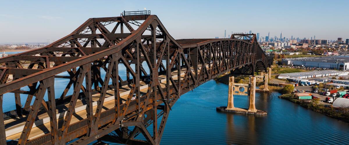 A large steel bridge spanning a river with a city skyline in the background.
