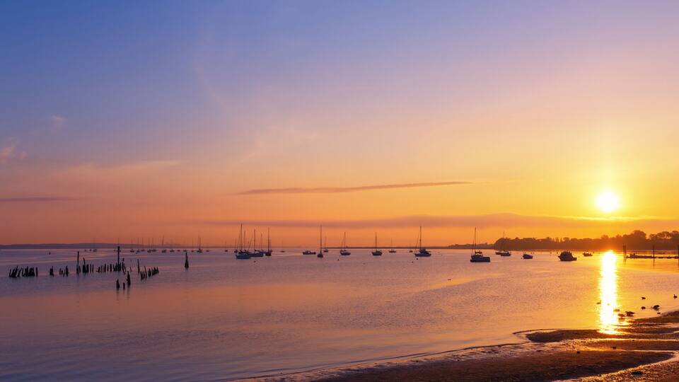 A sunset over a calm harbor with boats and a pier.