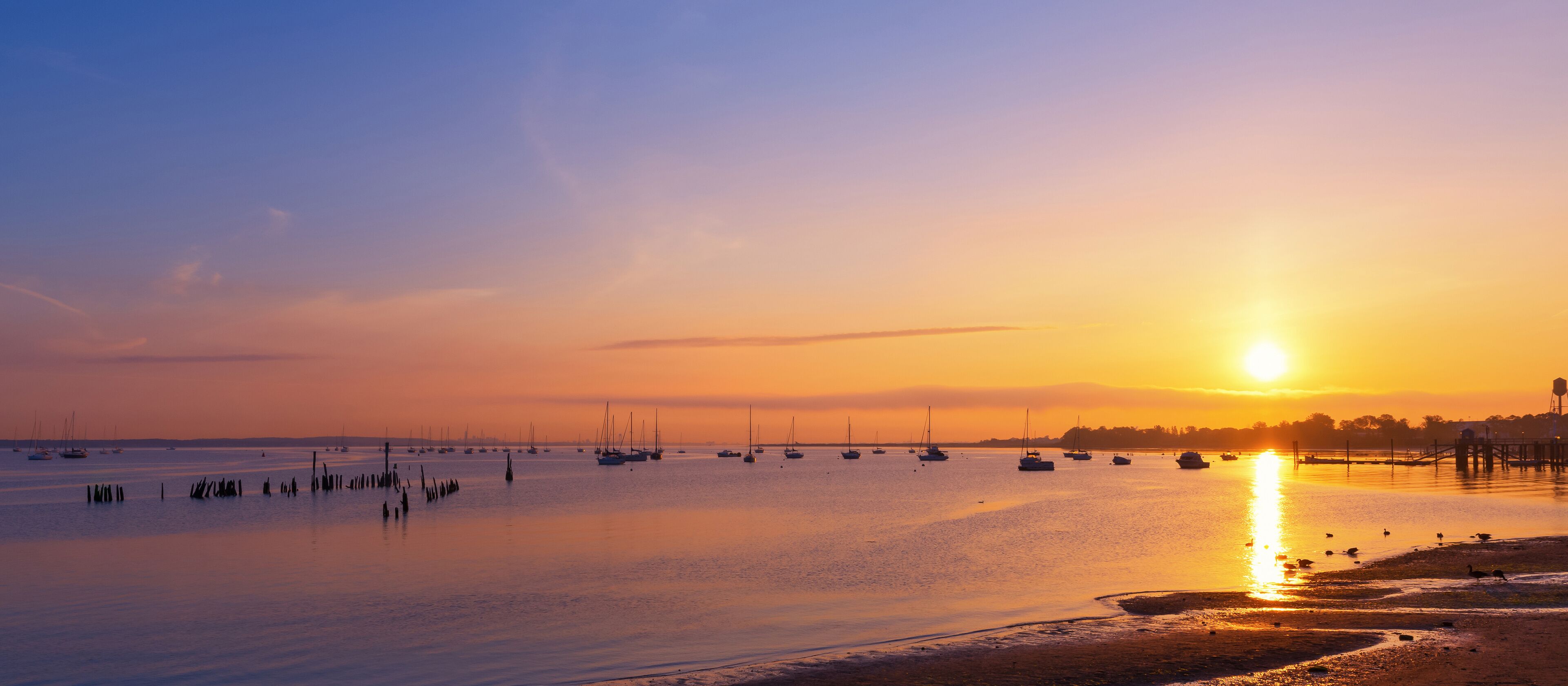 A sunset over a calm harbor with boats and a pier.