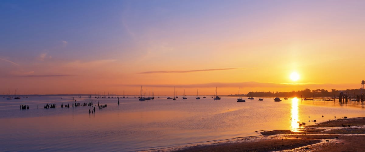 A sunset over a calm harbor with boats and a pier.