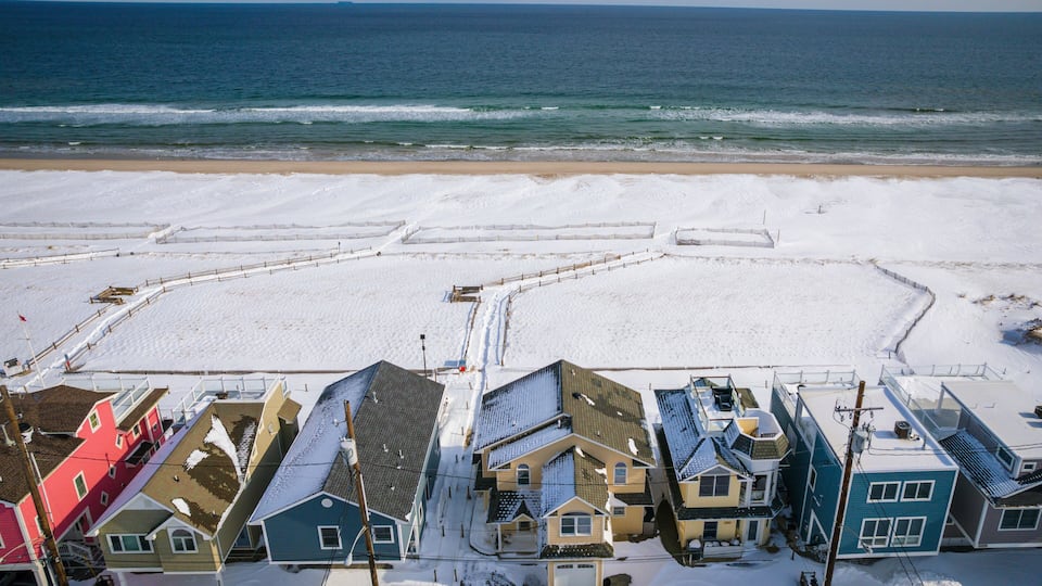A snowy beach with houses and a clear view of the ocean.