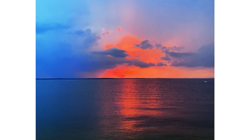 A sunset over a calm sea with a beach in the foreground.