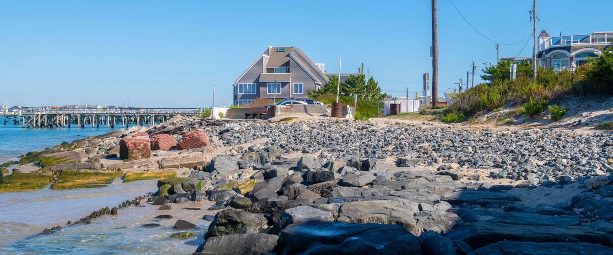 A rocky shoreline with a house and a pier in the background.