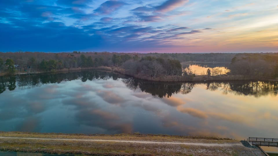 A tranquil lake with a wooden dock, surrounded by trees and a clear sky.