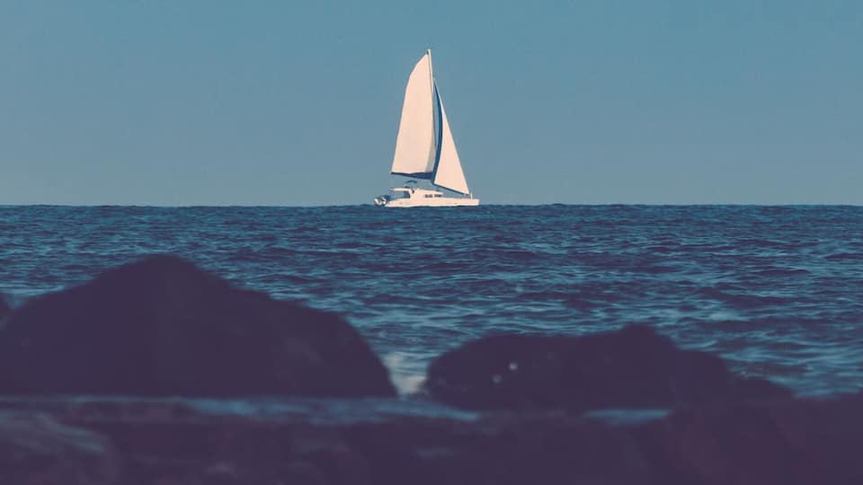 A sailboat on a calm sea with waves in the foreground.