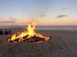 En strand med en eldstad i sanden och människor som sitter runt den.