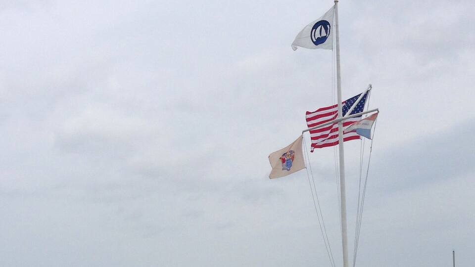 A wooden pier extending into a body of water with two flags on a pole.