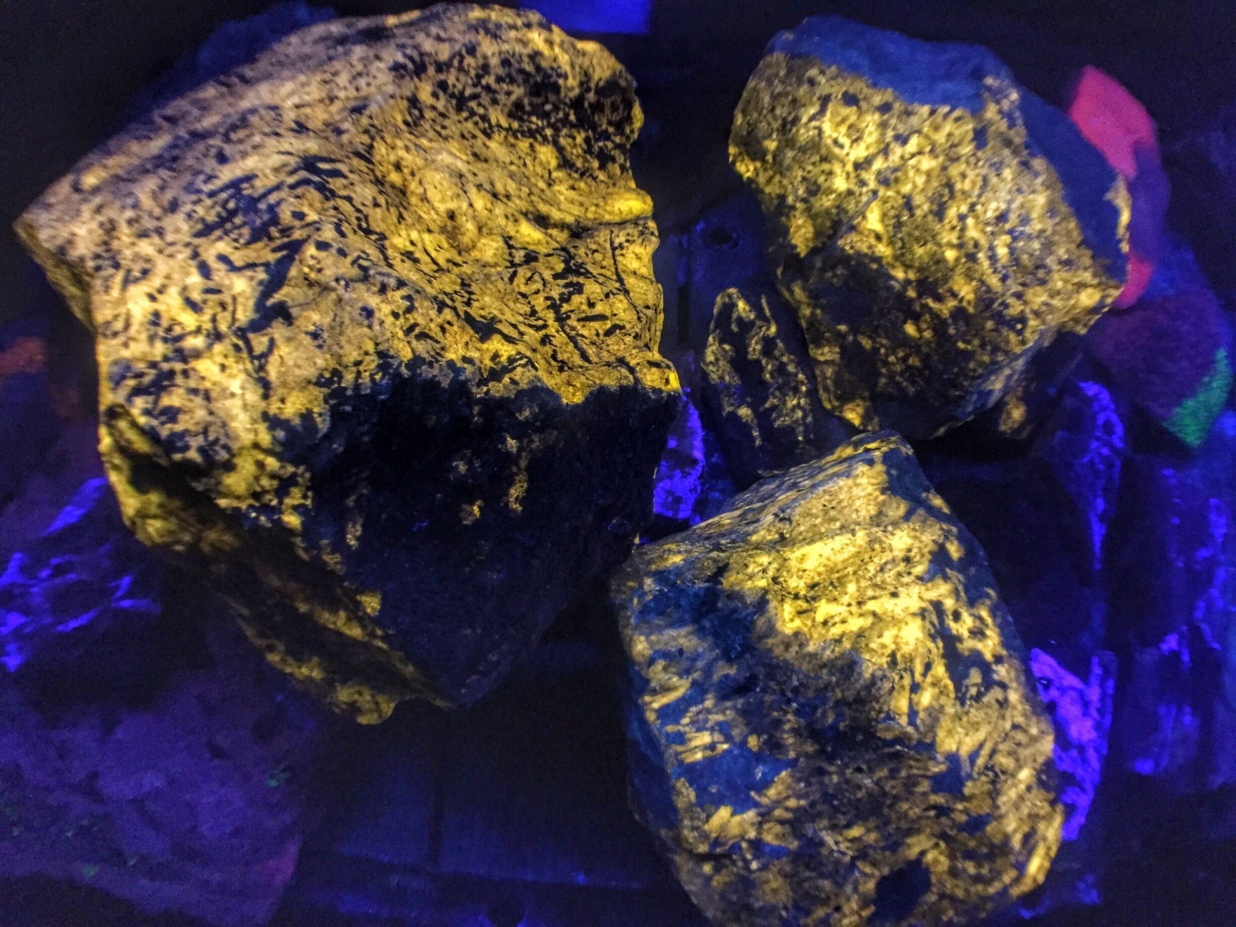 Three large, rough-textured rocks with a golden hue, illuminated by blue lighting.