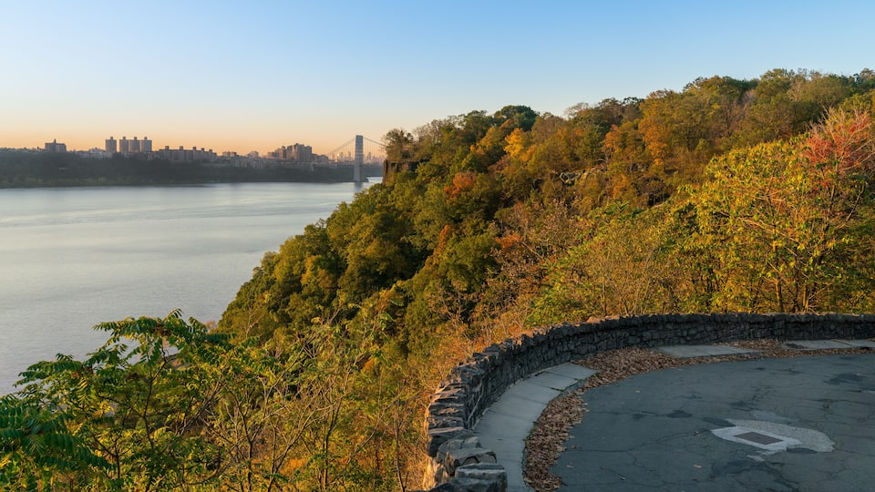 A scenic overlook with a view of a river, a stone wall, and a bridge in the distance.