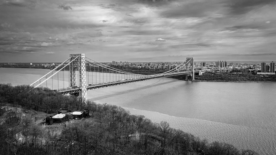 A suspension bridge spanning a river with a cityscape in the background.