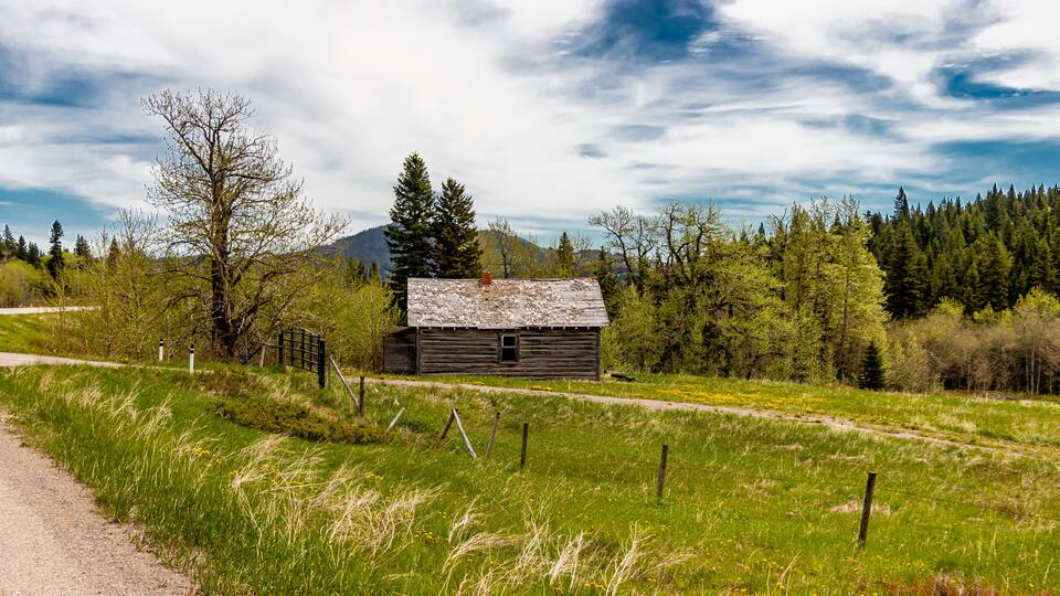 A rustic wooden cabin in a lush green field with a mountain in the background.