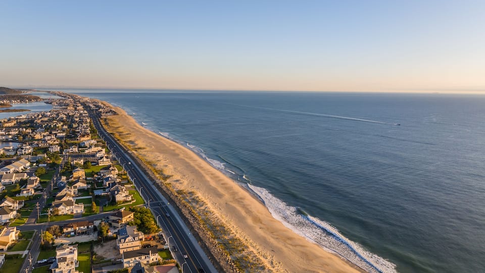 A coastal town with a long beach, a road parallel to the shore, and a clear sky.