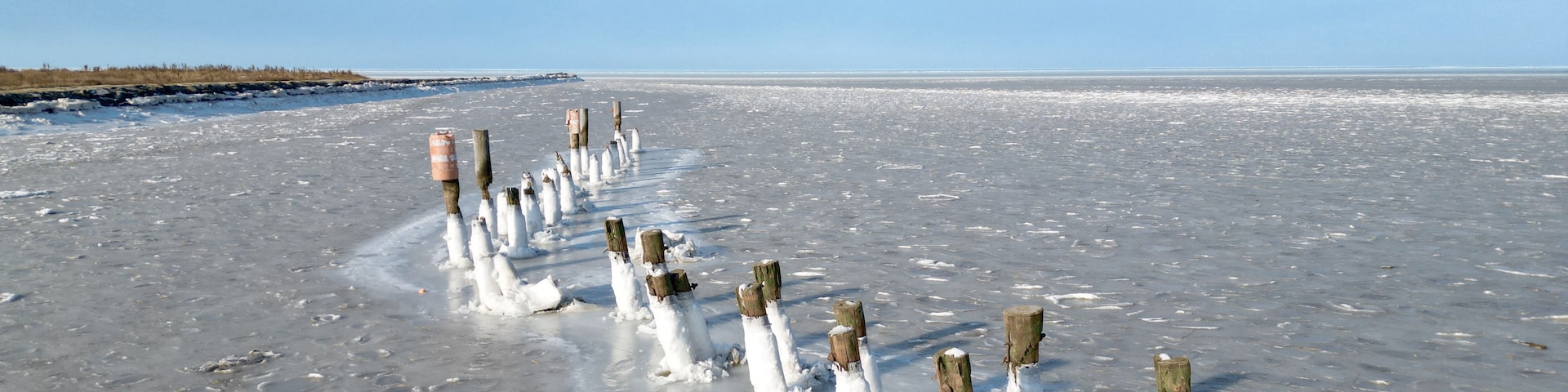 Un paisaje helado con postes de madera y huellas en la nieve.