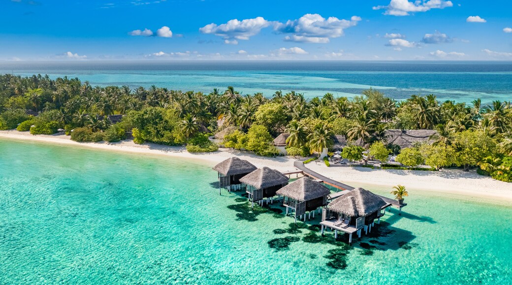 Aerial view of Maldives island, luxury water villas resort and wooden pier. Beautiful sky and ocean lagoon beach background. Summer vacation holiday and travel concept. Paradise aerial landscape pano