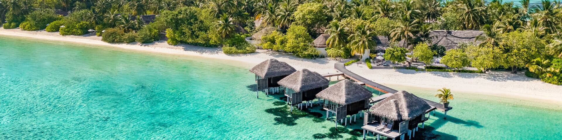 Aerial view of Maldives island, luxury water villas resort and wooden pier. Beautiful sky and ocean lagoon beach background. Summer vacation holiday and travel concept. Paradise aerial landscape pano