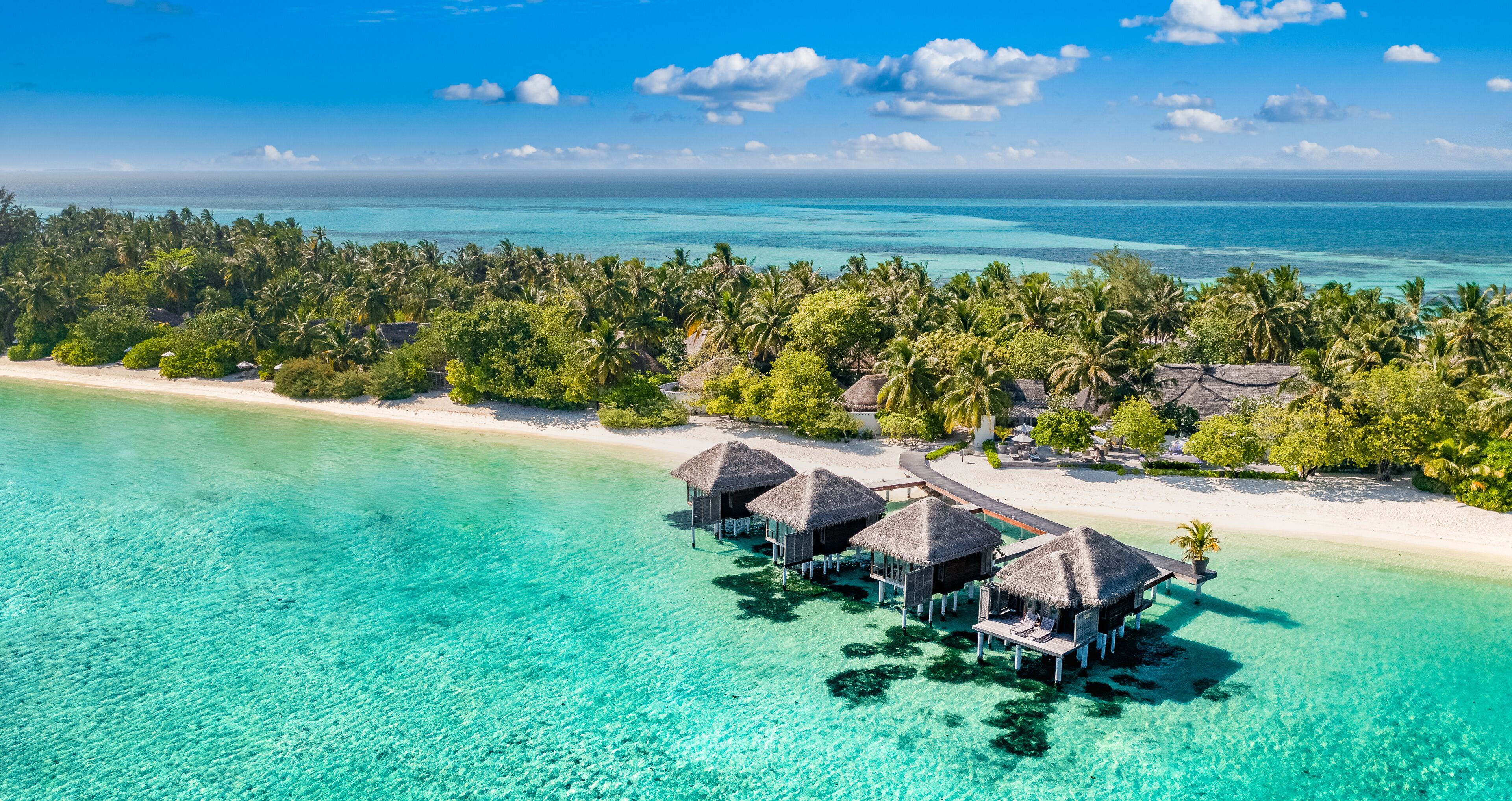 An aerial view of a tropical island resort with overwater bungalows and a clear turquoise sea.