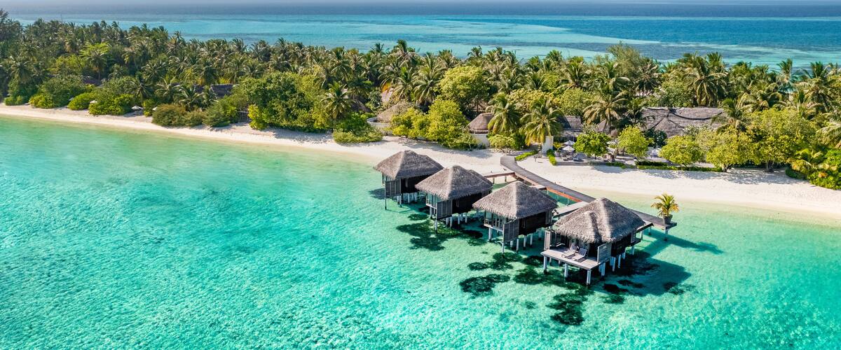 An aerial view of a tropical island resort with overwater bungalows and a clear turquoise sea.