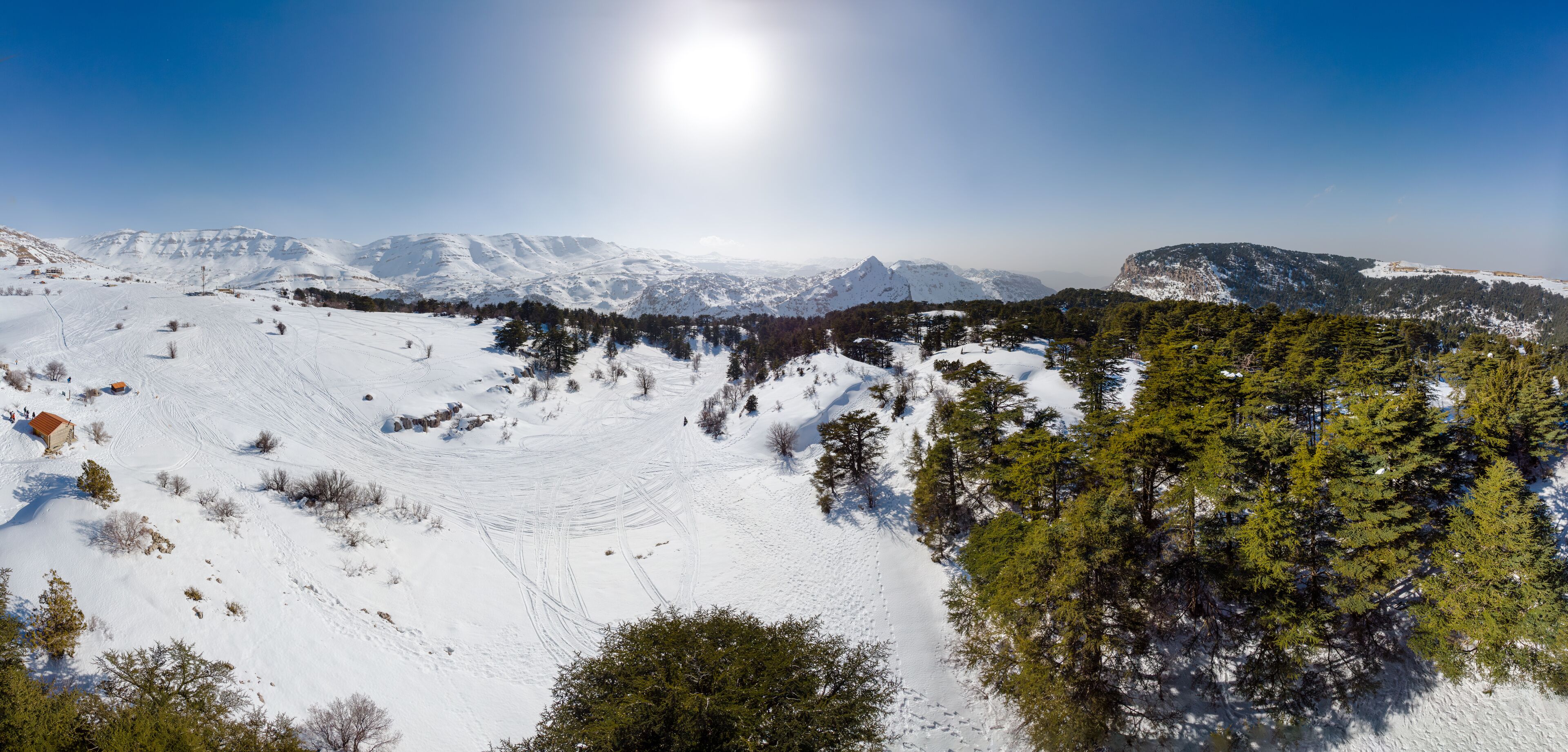 A snow-covered mountain landscape with clear skies and a bright sun.