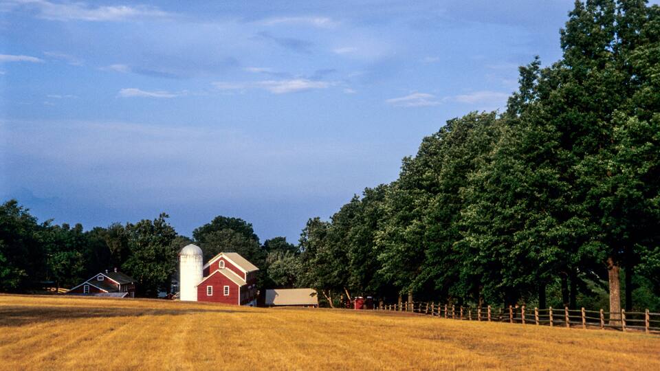 A red barn with a silo, surrounded by a wooden fence and trees.
