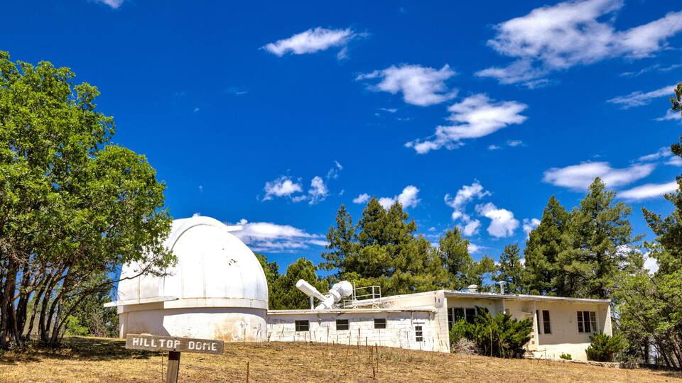 A white dome structure labeled "HILTIPE DOME" with a telescope, surrounded by trees and a clear blue sky.