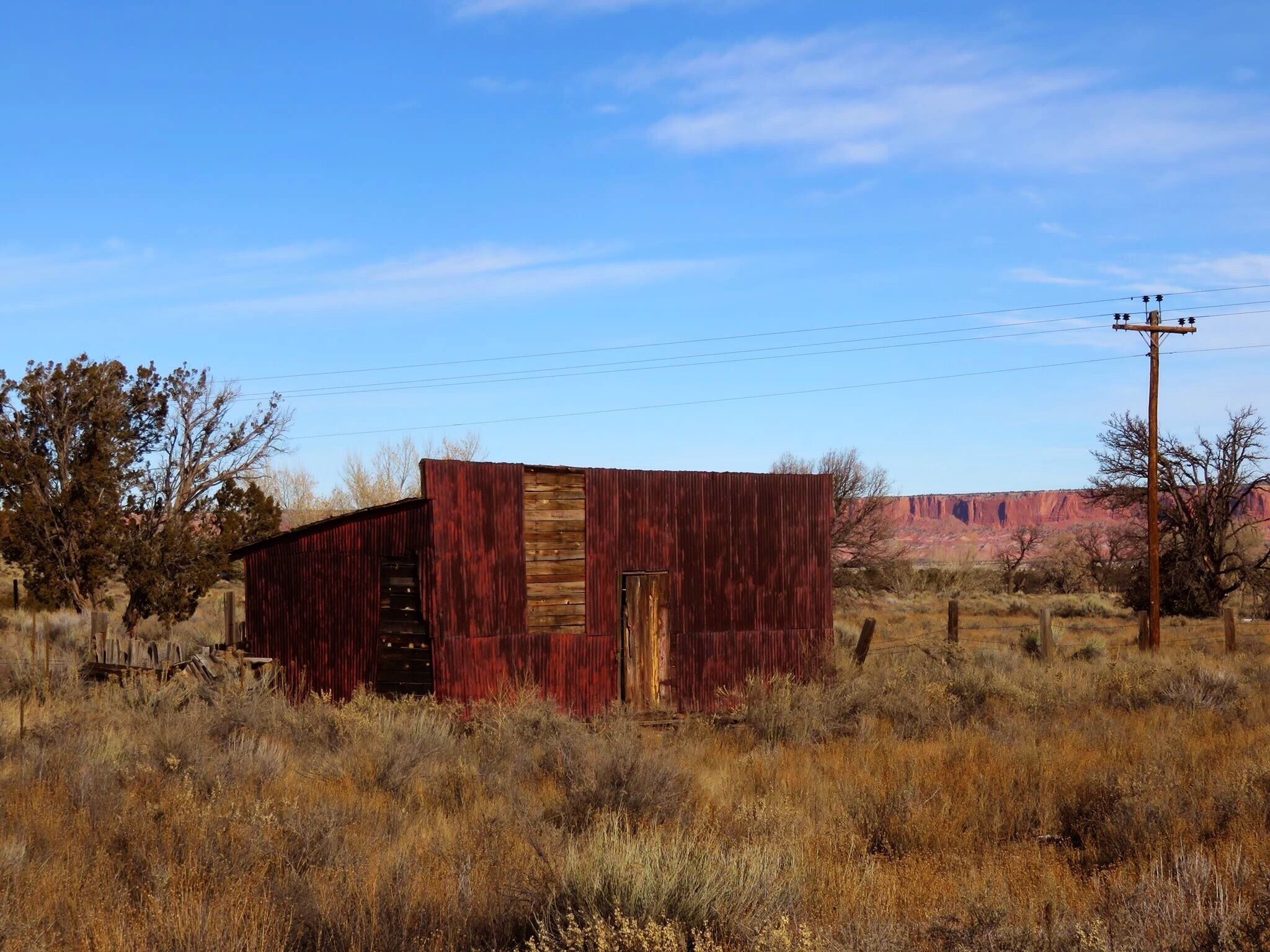 A red barn in a dry grass field with a clear blue sky and distant red rock formations.