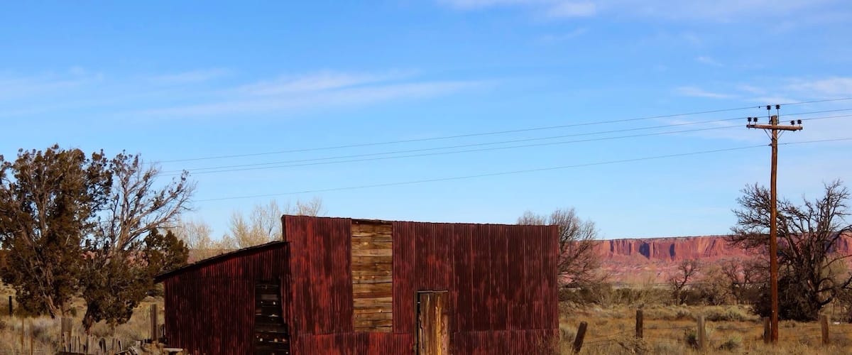 A red barn in a dry grass field with a clear blue sky and distant red rock formations.