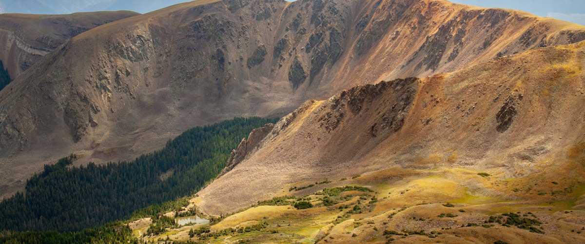 A mountainous landscape with a valley, a small lake, and a dense forest area.