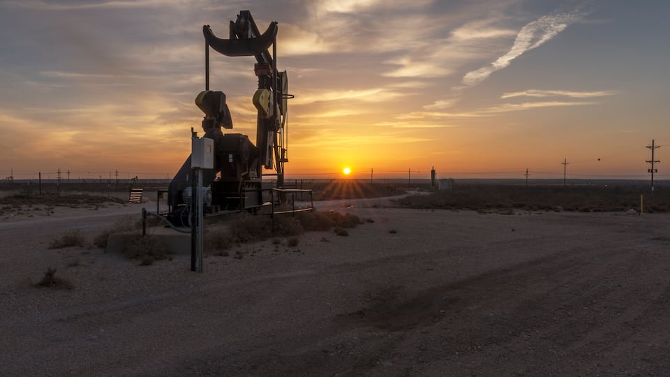 A desert landscape with a large oil rig silhouetted against a sunset.