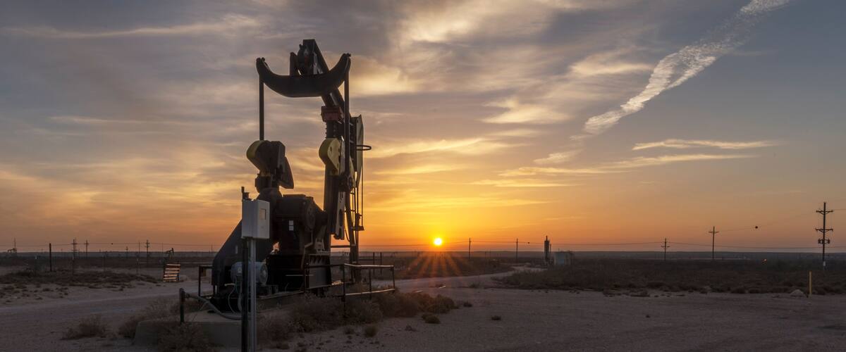A desert landscape with a large oil rig silhouetted against a sunset.