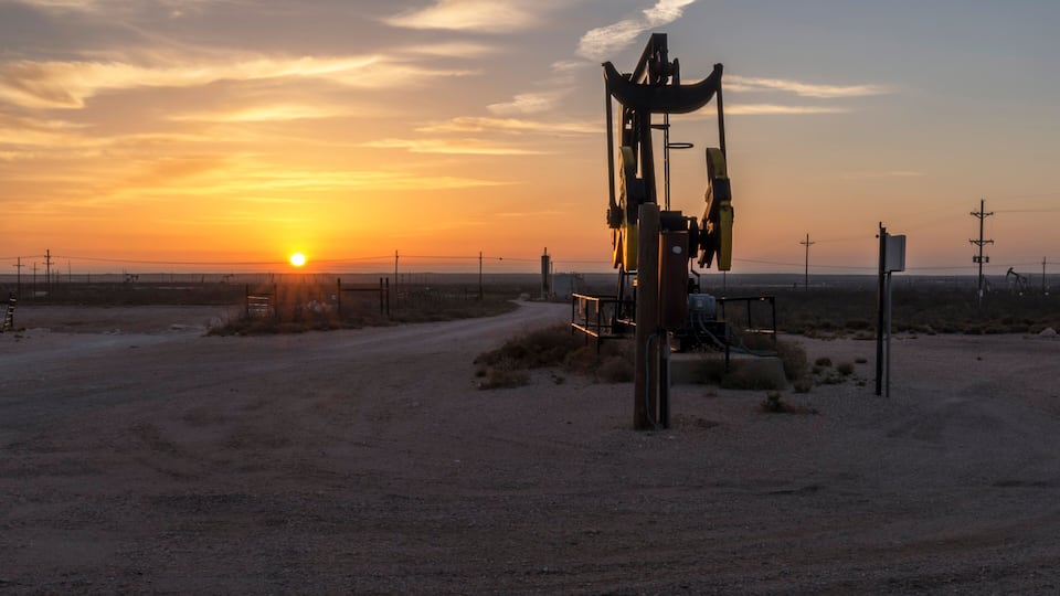A sunset over a desert landscape with a drilling rig in the foreground.