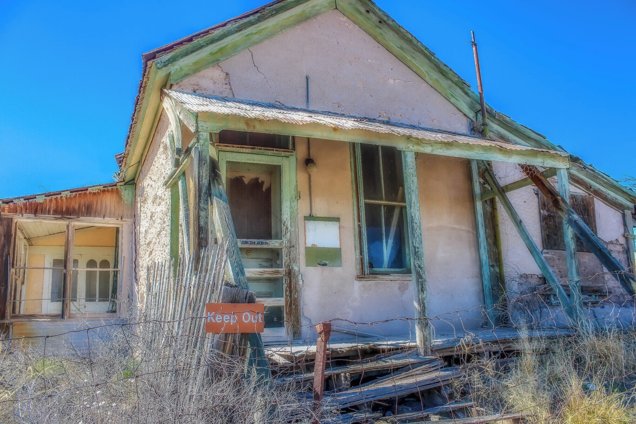 A dilapidated house with a 'Keep Out' sign, overgrown vegetation, and a collapsed roof.