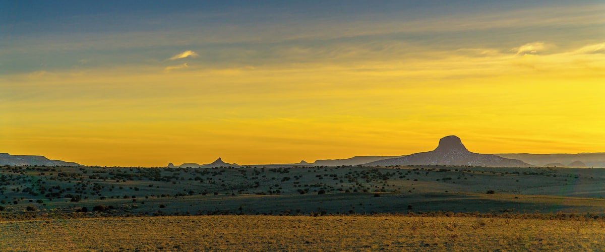 A landscape with a prominent mountain silhouette against a sunset sky.