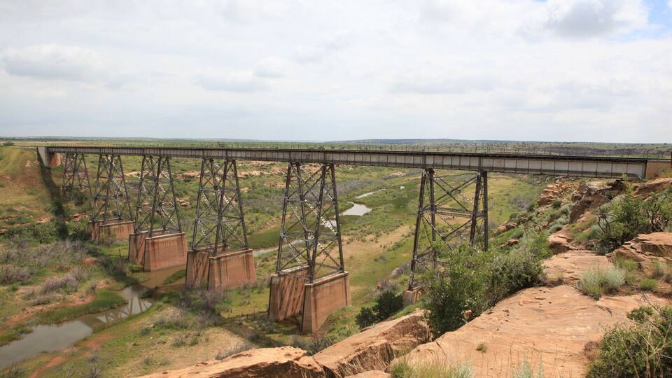 A large steel bridge spanning a river in a dry, hilly landscape.