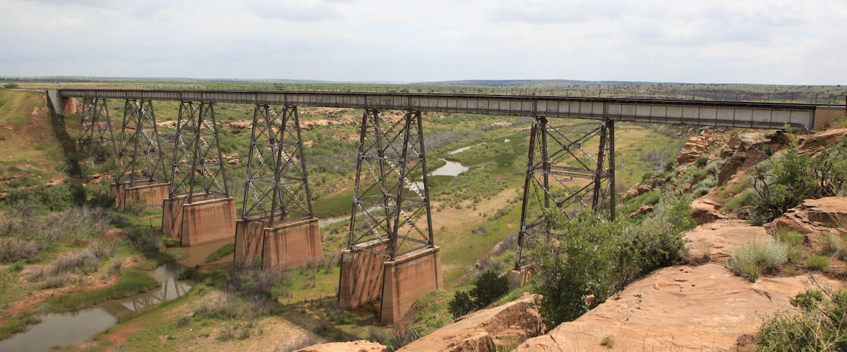 A large steel bridge spanning a river in a dry, hilly landscape.