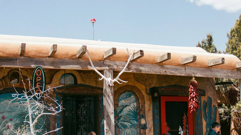 A rustic building with a wooden roof, a red door, and a sign that reads "OPEN".