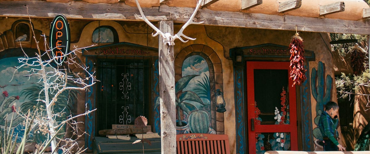 A rustic building with a wooden roof, a red door, and a sign that reads "OPEN".