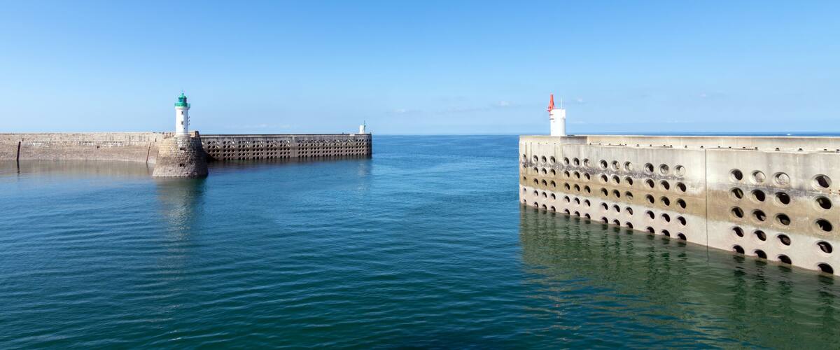 A lighthouse and pier extending into calm blue waters under a clear sky.
