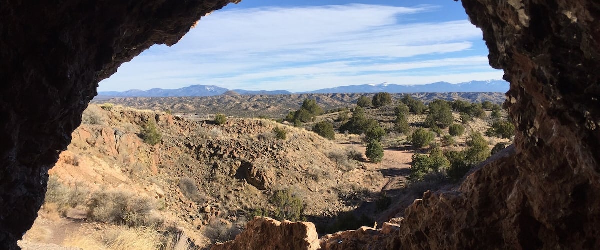 A rocky terrain with a cave entrance, a dirt path, and distant mountains.
