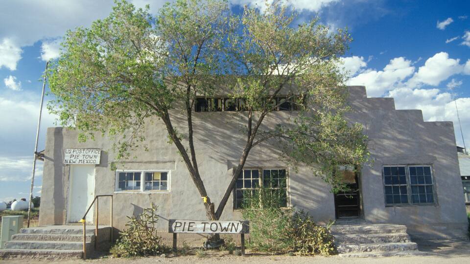 A historic US Post Office in Pie Town, New Mexico, with a large tree in front and a clear blue sky.