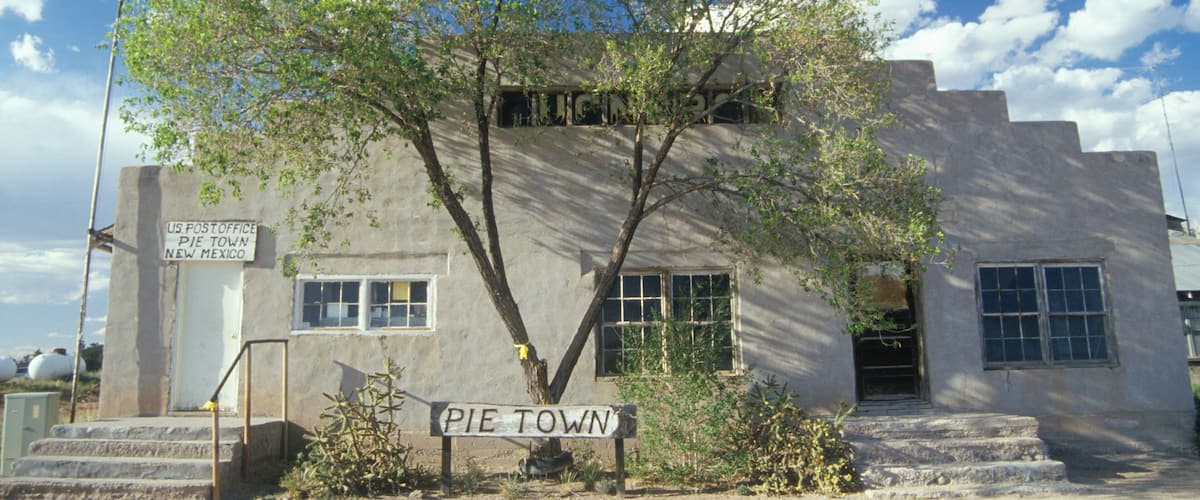 A historic US Post Office in Pie Town, New Mexico, with a large tree in front and a clear blue sky.