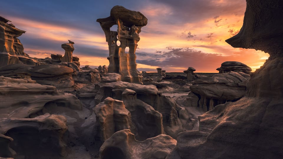 A desert landscape with rock formations and a sunset.