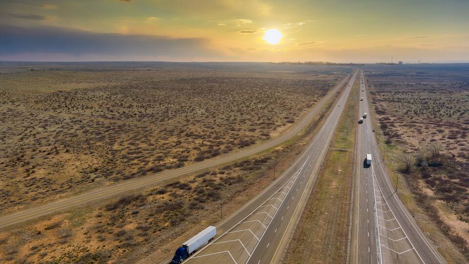 A highway in a desert landscape with sparse vegetation and a clear sky.