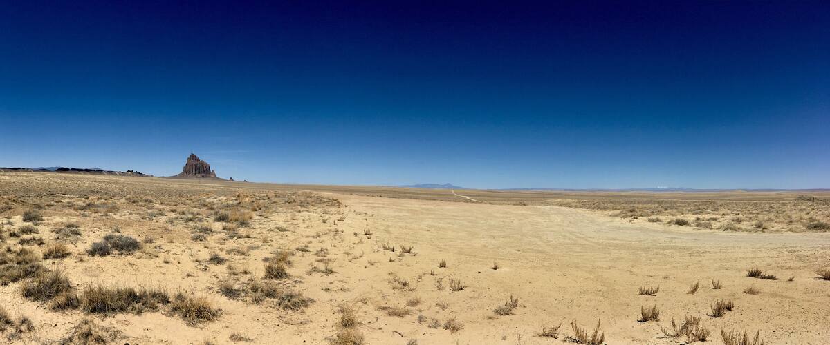 A desert landscape with sparse vegetation and a prominent rocky hill in the distance.
