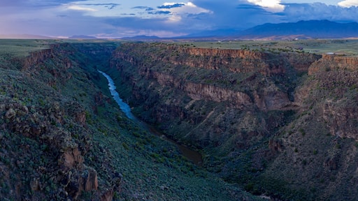 A canyon with a river flowing through it, surrounded by mountains and a cloudy sky.