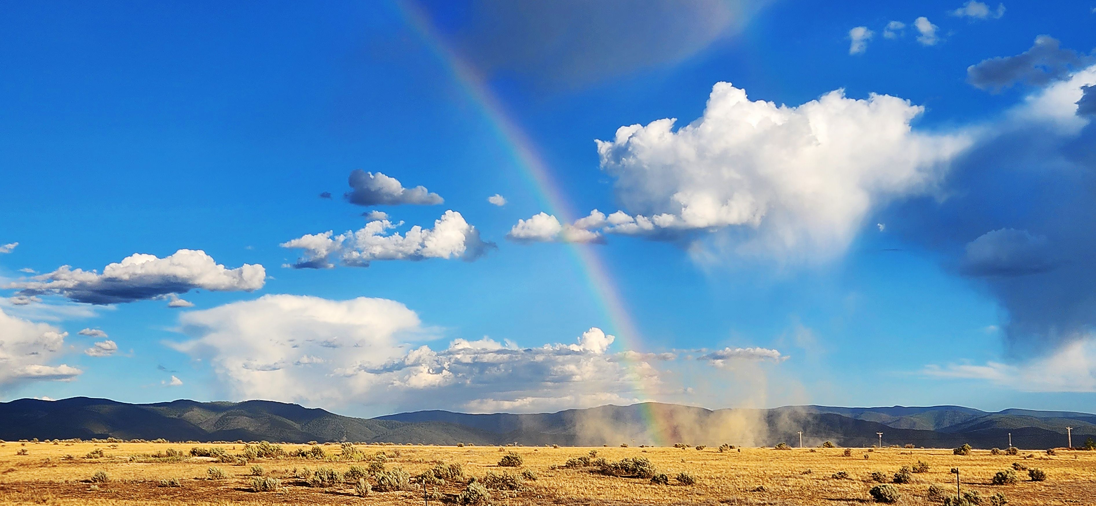 A landscape with a rainbow, mountains, and a clear sky.
