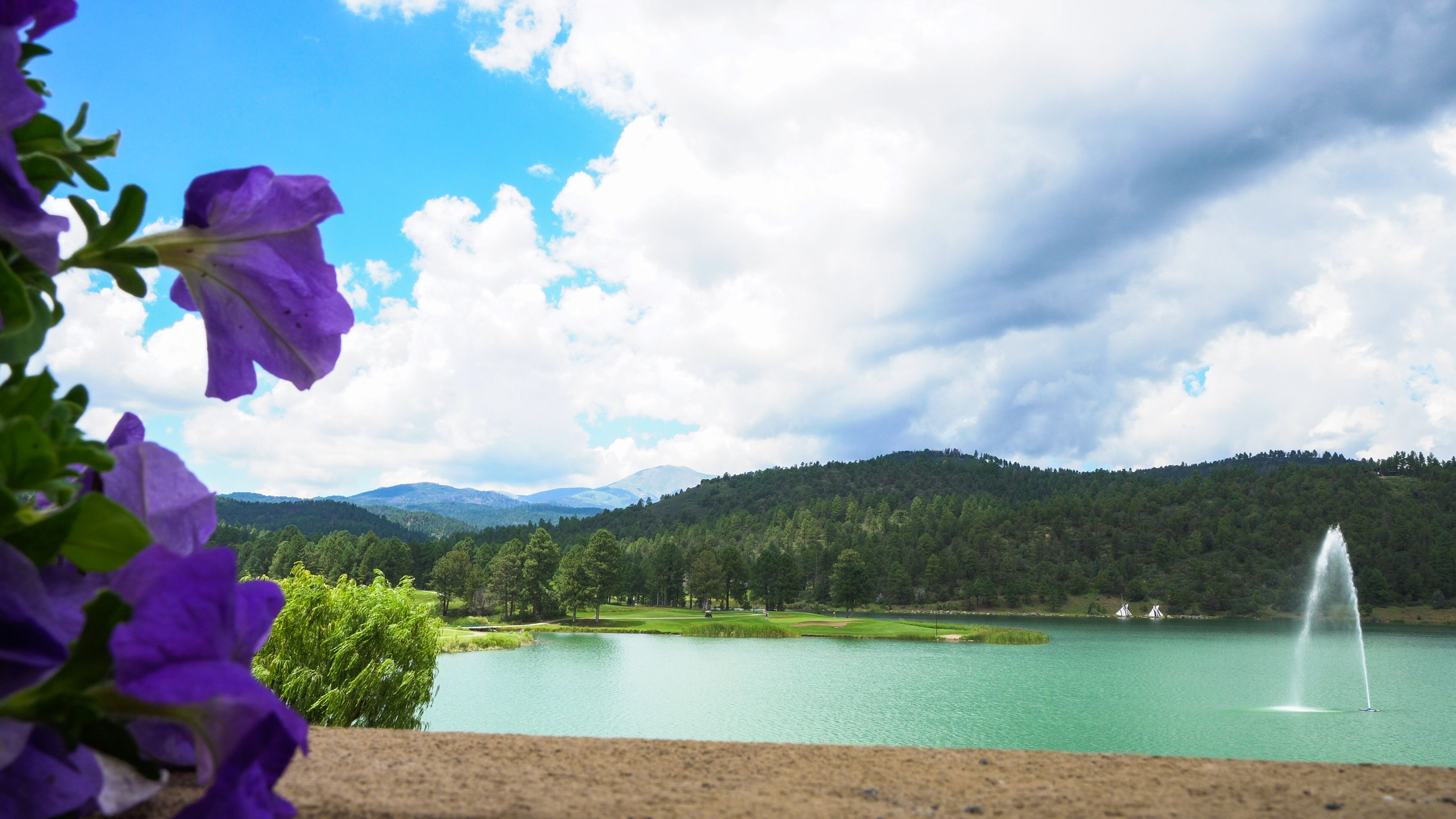 A lake with a fountain, surrounded by mountains and a cloudy sky.
